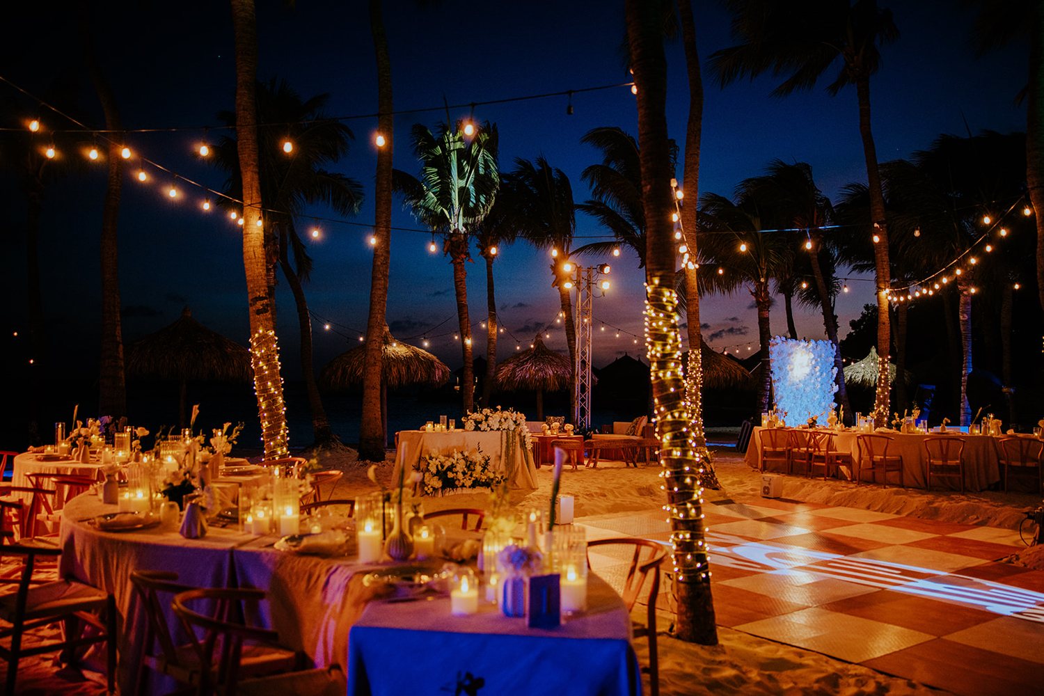 Reception tables beneath illuminated palm trees at night