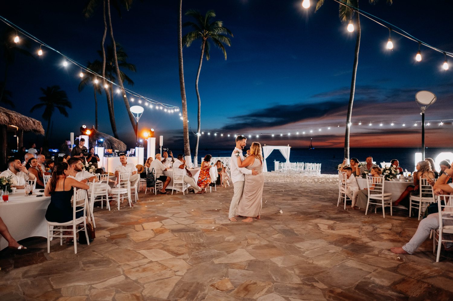 A beach reception at dusk beneath string lights