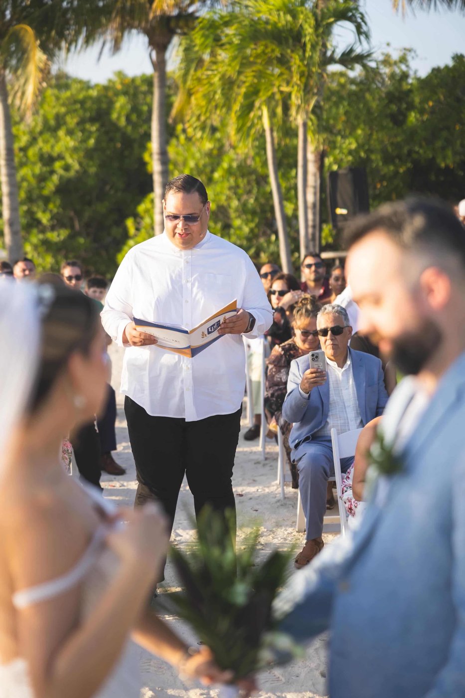 Ruuben wearing a headset and reading from a booklet at an outdoor wedding